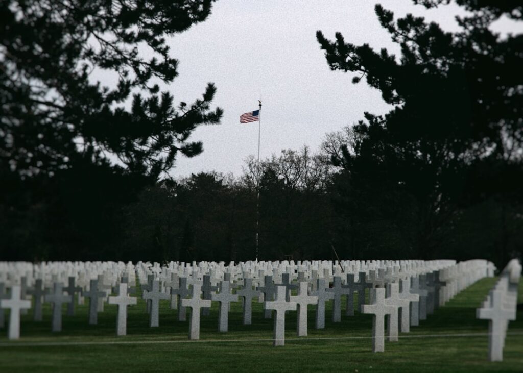 White grave markers and an American flag in a military cemetery, honoring Memorial Day 2027